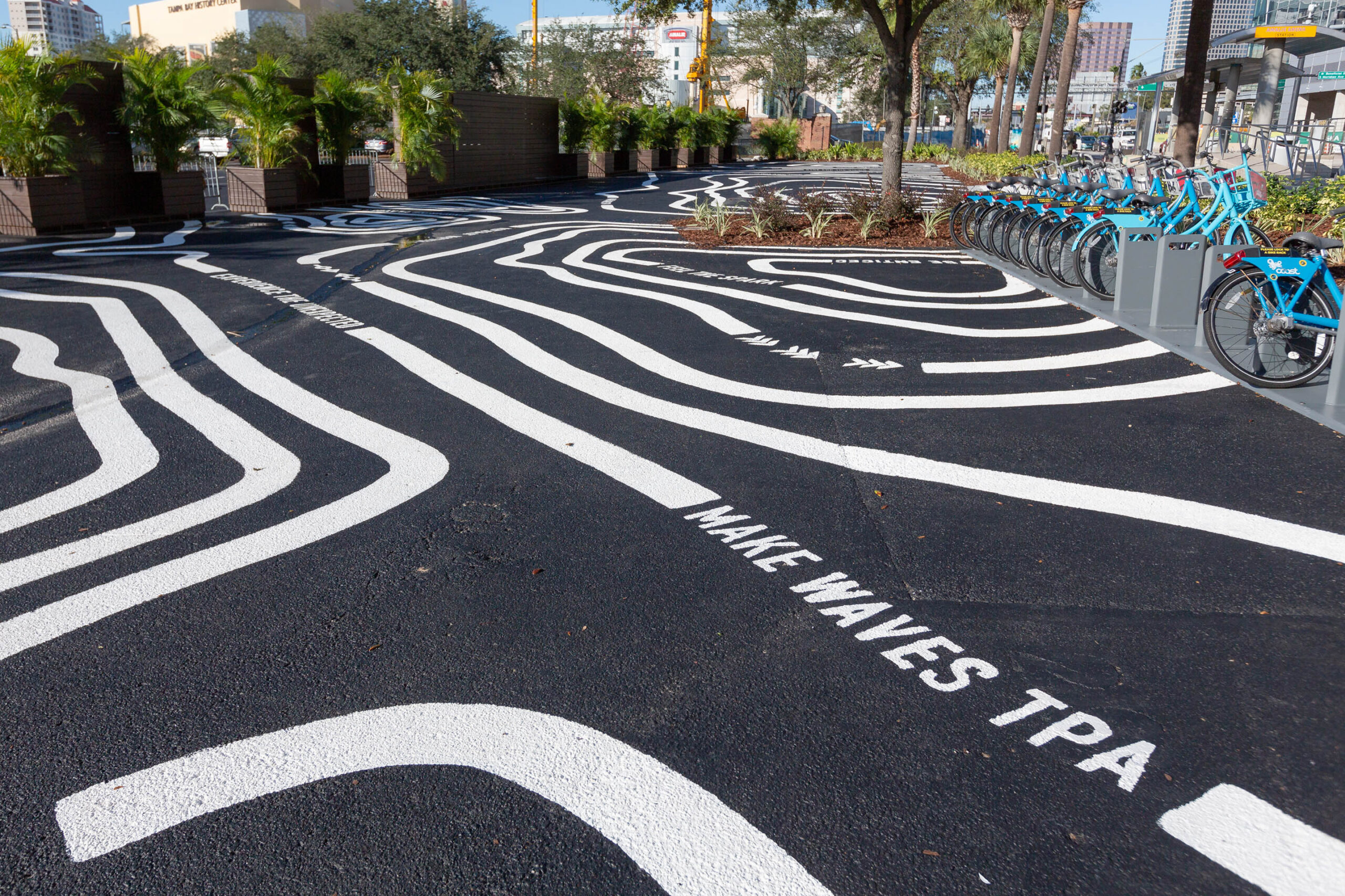 Painted parking lot mural with topographic lines and the Make Waves TPA slogan at Water Street Tampa